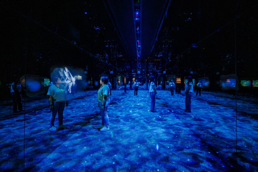 Blue corridor with reflective screens on each side and a projected array of particles on the floor.